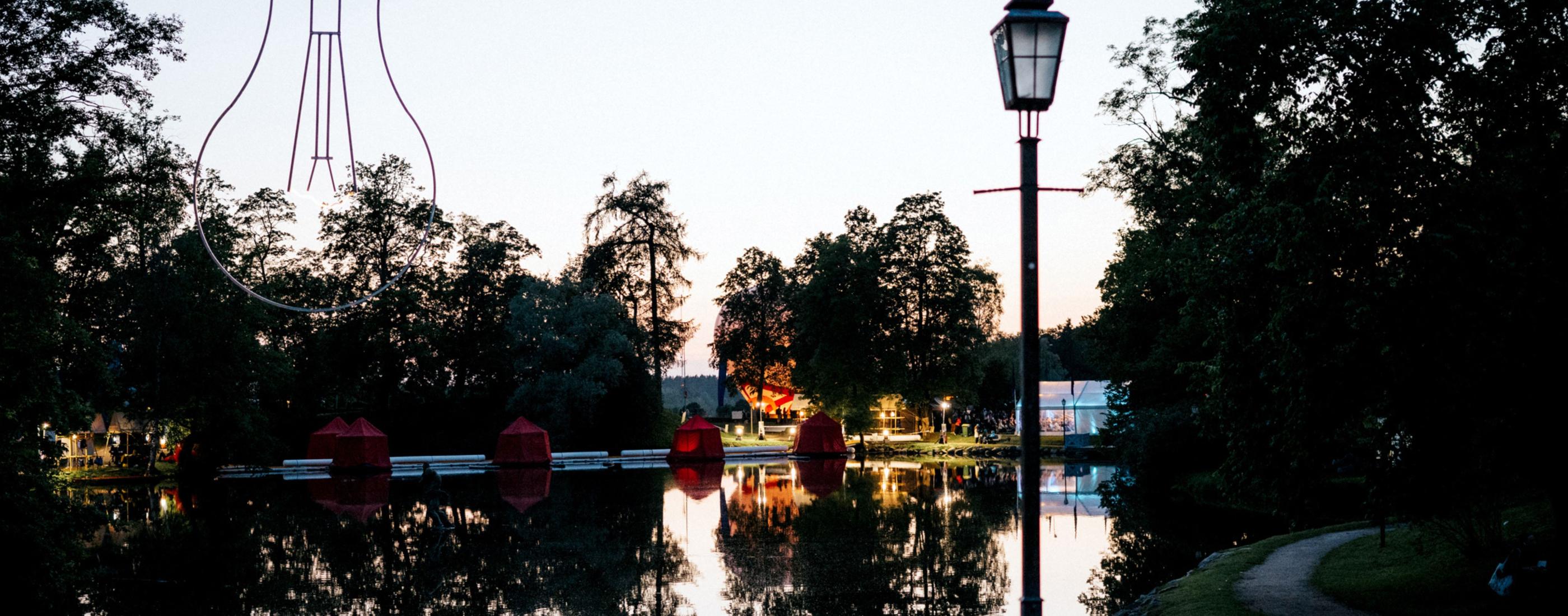 Krēslas stunda redzams Cēsu Pils parka dīķis ar skatuvi uz ūdens un festivāla dekorācijām